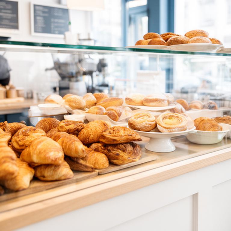 Glass pastry counter with croissants and buns in a bright local coffee shop